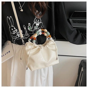 Detail view of cream pleated bucket bag with colorful round bead handle and enjoy text