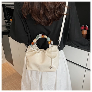 Detail of a pleated bucket bag featuring multi-colored beaded handles and drawstring closure