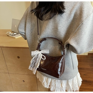 Détail d'un sac bandoulière en cuir verni marron avec nœud en dentelle et chaîne perle