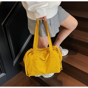 Detail of a bright yellow nylon tote bag with drawstring feature on a wooden staircase