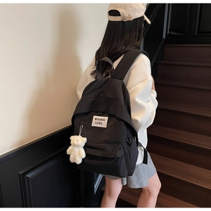 Close-up of minimalist black backpack with logo patch and white teddy bear pendant