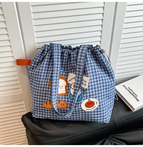 Detail view of blue checkered canvas tote bag with embroidered cartoon patches and drawstring
