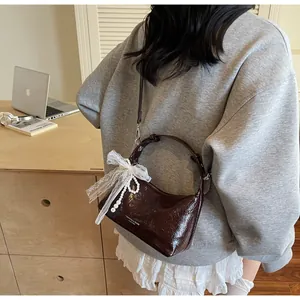 Détail du sac hobo marron foncé avec nœud en dentelle et chaîne de perles sur bureau