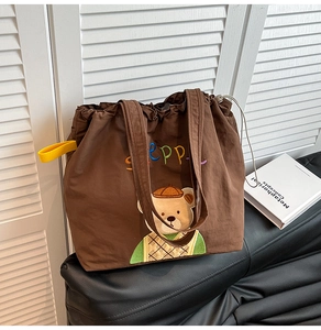 Detail of a large brown canvas tote bag with embroidered bear and rainbow lettering