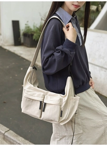 Outdoor shot of a beige canvas messenger bag featuring dual front pockets and wide strap