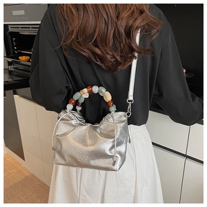 Detail of silver pleated bucket bag with beaded handle worn as a crossbody on a model