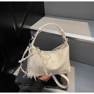 Détail d'un sac à main en cuir froissé crème avec nœud en perles et breloque en dentelle