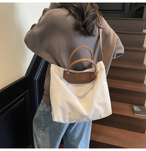Detail of off-white canvas tote bag featuring brown leather trim and metal snap closure