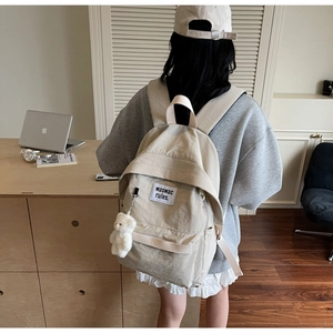 Vista dettagliata dello zaino in tela beige con ciondolo a orso e toppa waswac