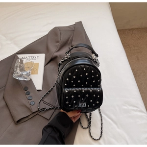 Detailed close-up of a quilted black leather mini backpack with silver metal studs and chain