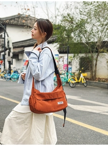 Detail of orange nylon dumpling bag showing side elastic pocket and adjustable strap