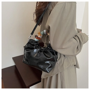 Detail of black patent leather bucket bag with colorful acrylic bead handle and drawstrings
