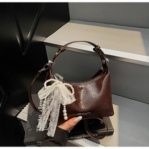 Détail d'un sac à main marron foncé brillant avec nœud en dentelle blanche et perles