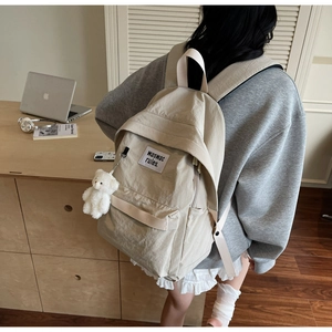 Dettaglio dello zaino in tela beige con ciondolo a forma di orsetto e logo minimalista