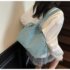 Detail of light blue nylon bucket bag showing drawstring closure and large front pocket