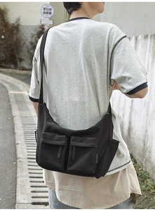 Detail view of black nylon crossbody bag with dual front flap pockets and wide strap