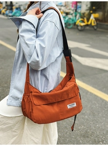 Detail view of burnt orange nylon crossbody bag with side drawstring and woven label