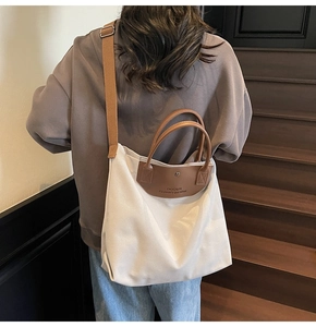 Detail of the white canvas tote bag showing the brown leather patch and dual handles