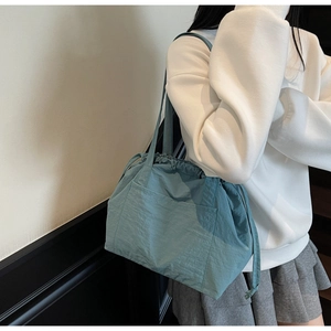 Detail of teal nylon drawstring tote bag with large front pocket on a female model