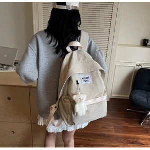 Detail of off-white canvas backpack featuring a plush bear charm and letter patch