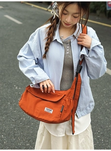 Outdoor street shot of an orange nylon crossbody bag paired with a denim jacket