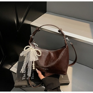 Détail d'un sac à main en cuir marron foncé brillant avec nœud dentelle et perles