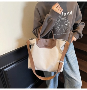 Close-up of the beige canvas tote bag with brown leather accents and logo detail