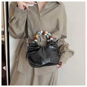Detail of glossy black pleated bucket bag with colorful beaded handle and lettering