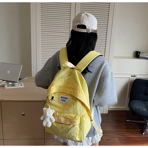 Dettaglio dello zaino in nylon giallo con ciondolo a orsetto bianco e logo sul retro