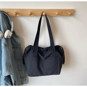 Detailed view of black nylon tote bag with drawstring side and front pocket on a hanger
