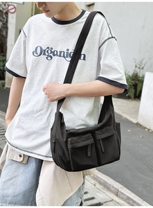 Detail shot of a black nylon crossbody bag featuring front pockets and wide shoulder strap