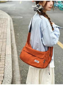 Detailed macro view of orange nylon dumpling bag showing adjustable black strap and fabric label
