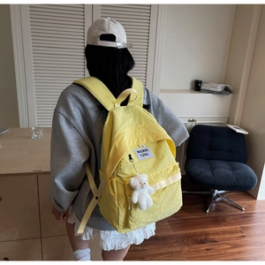 Dettaglio dello zaino in nylon giallo con un grazioso orsetto di peluche bianco laterale