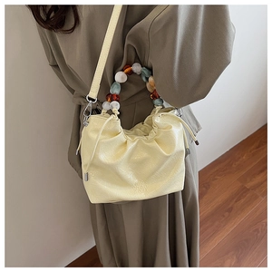 Detail of light yellow quilted bucket bag featuring colorful beaded handle and drawstring