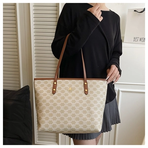 Detail of monogram tote bag with brown leather handles and golden logo pendant