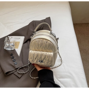 Detail of white quilted backpack with silver studs and metal chain strap on textured fabric