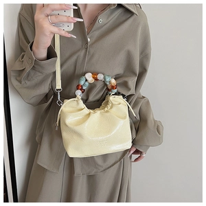 Detail of cream pleated cloud bag featuring colorful beaded round handle and long strap