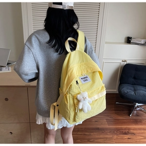 Dettaglio di zaino in nylon giallo con etichetta logo bianca e ciondolo a forma di orso
