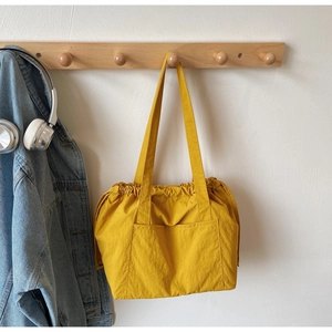 Detail of a bright yellow nylon drawstring tote bag with a front pocket and wide strap
