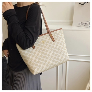 Close-up of cream canvas tote bag with brown leather trim and golden metal logo detail