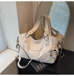 Détail du sac cabas crème avec clous en étoile et fermetures éclair sous la lumière