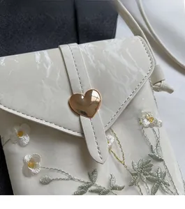 Détail d'un sac brodé blanc avec fermoir cœur doré et rabat à texture marbrée