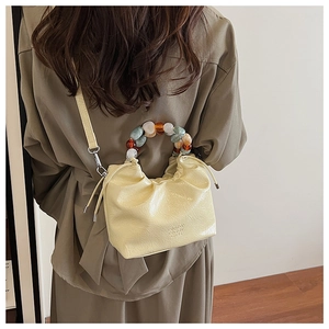 Detail of light yellow pleated bucket bag with multi-colored resin bead handle and strap