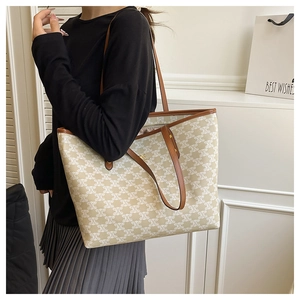 Close-up of beige monogram tote bag with brown leather trim worn by a model