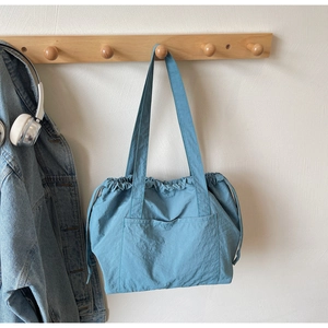 Blue nylon tote bag detail with drawstring closure and exterior pocket on a wooden hook