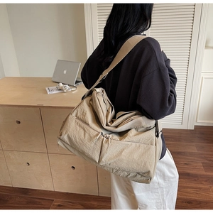 Detail view of the multi-zipper compartments and adjustable strap on a khaki nylon tote bag
