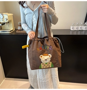 Detail of a brown canvas tote bag with cartoon bear embroidery and drawstring closure