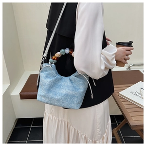 Detail of light blue pleated bucket bag with a colorful beaded handle and drawstring closure