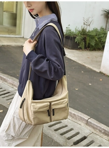 Detail of beige nylon crossbody bag with utility pockets and black zipper accent