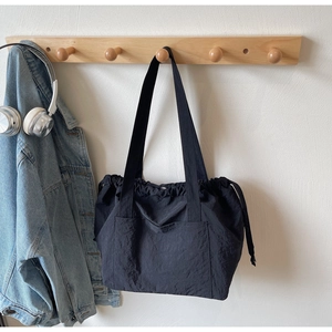 Detail of black nylon tote bag featuring side drawstrings and front pocket on hanger